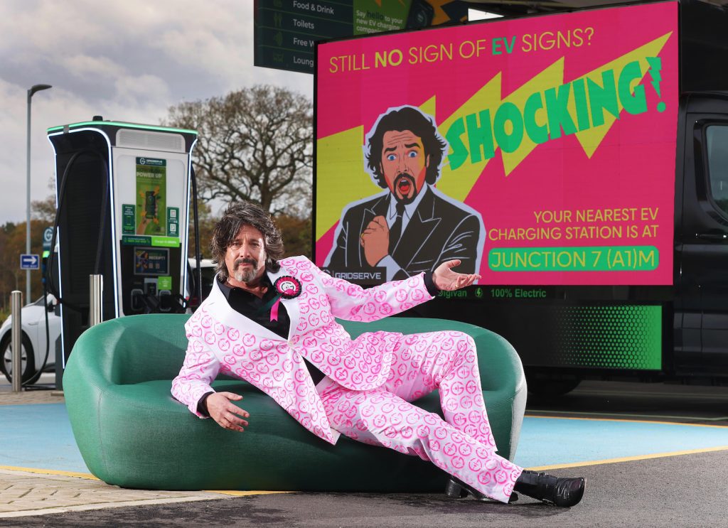 Laurence Llewelyn-Bowen reclines on a sofa in front of digital electric ad van